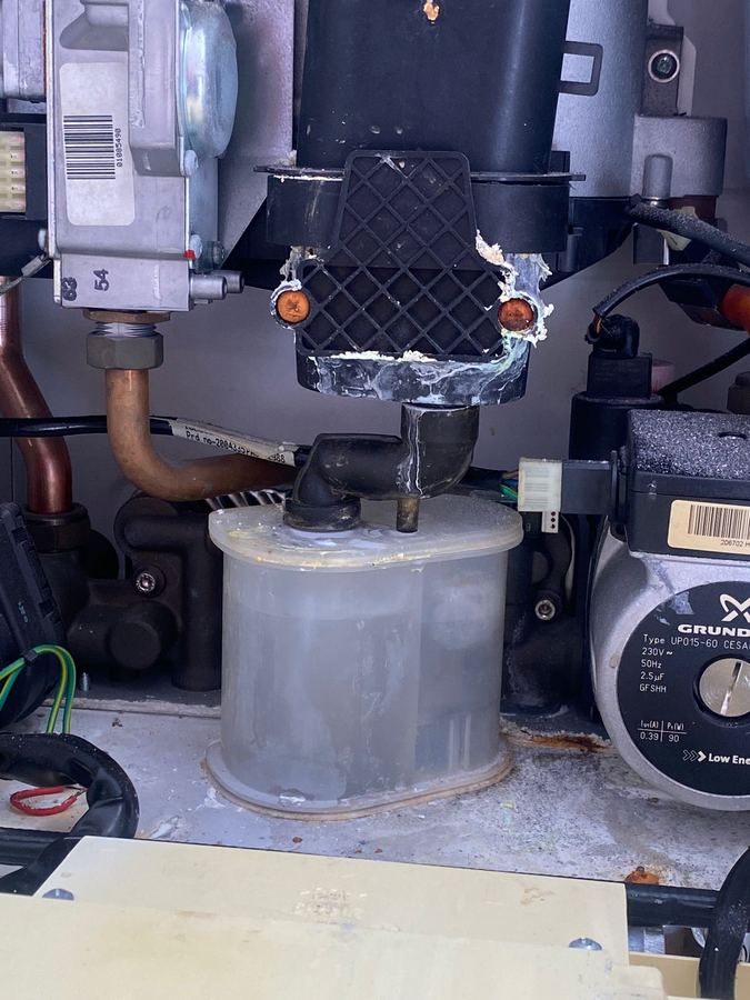 Inside an older boiler during a repair, showing the condensate trap, fan and pump